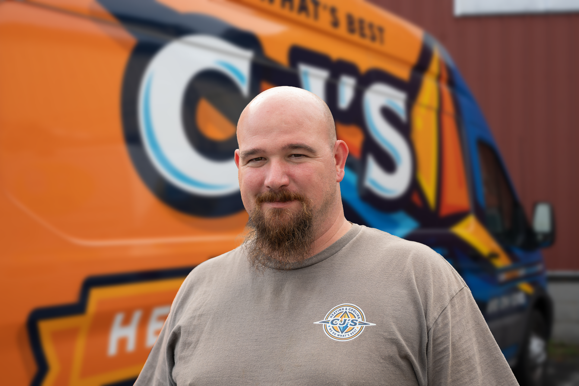 A bald man with a beard wearing a blue shirt that says ' carhartt ' on it