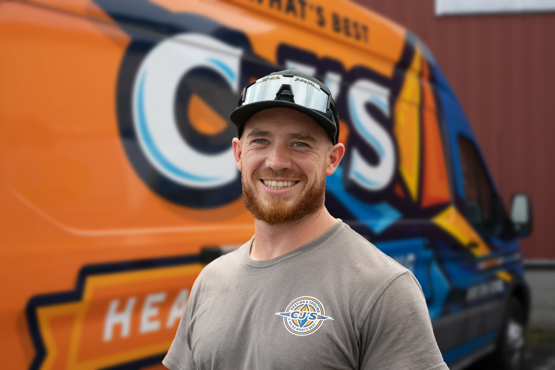 A man wearing a black hoodie and a beanie stands in front of a van that says heating and cooling