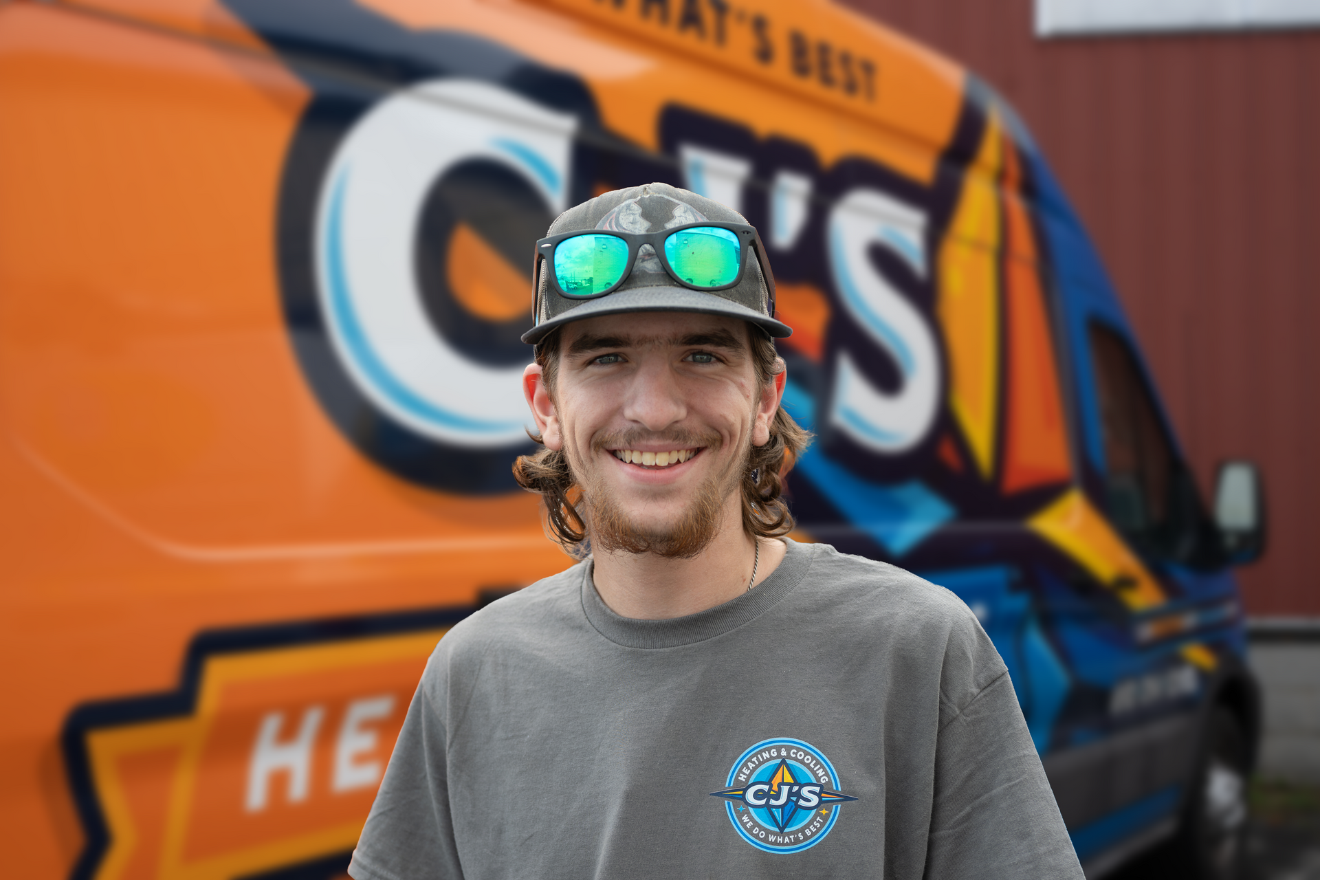 Man in black beanie and jacket smiling in front of a white van with orange and blue logo.