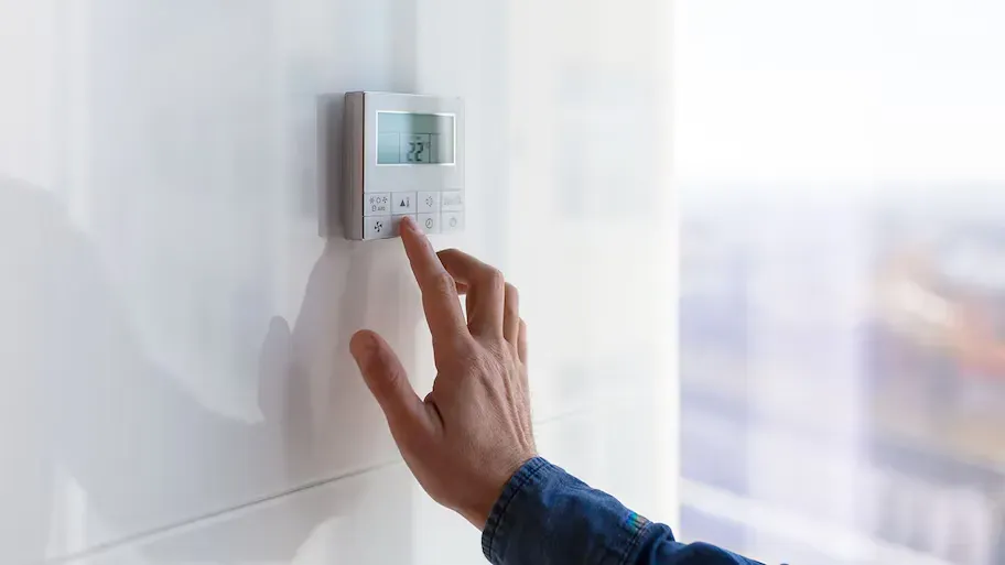 A person is adjusting a thermostat on a wall.