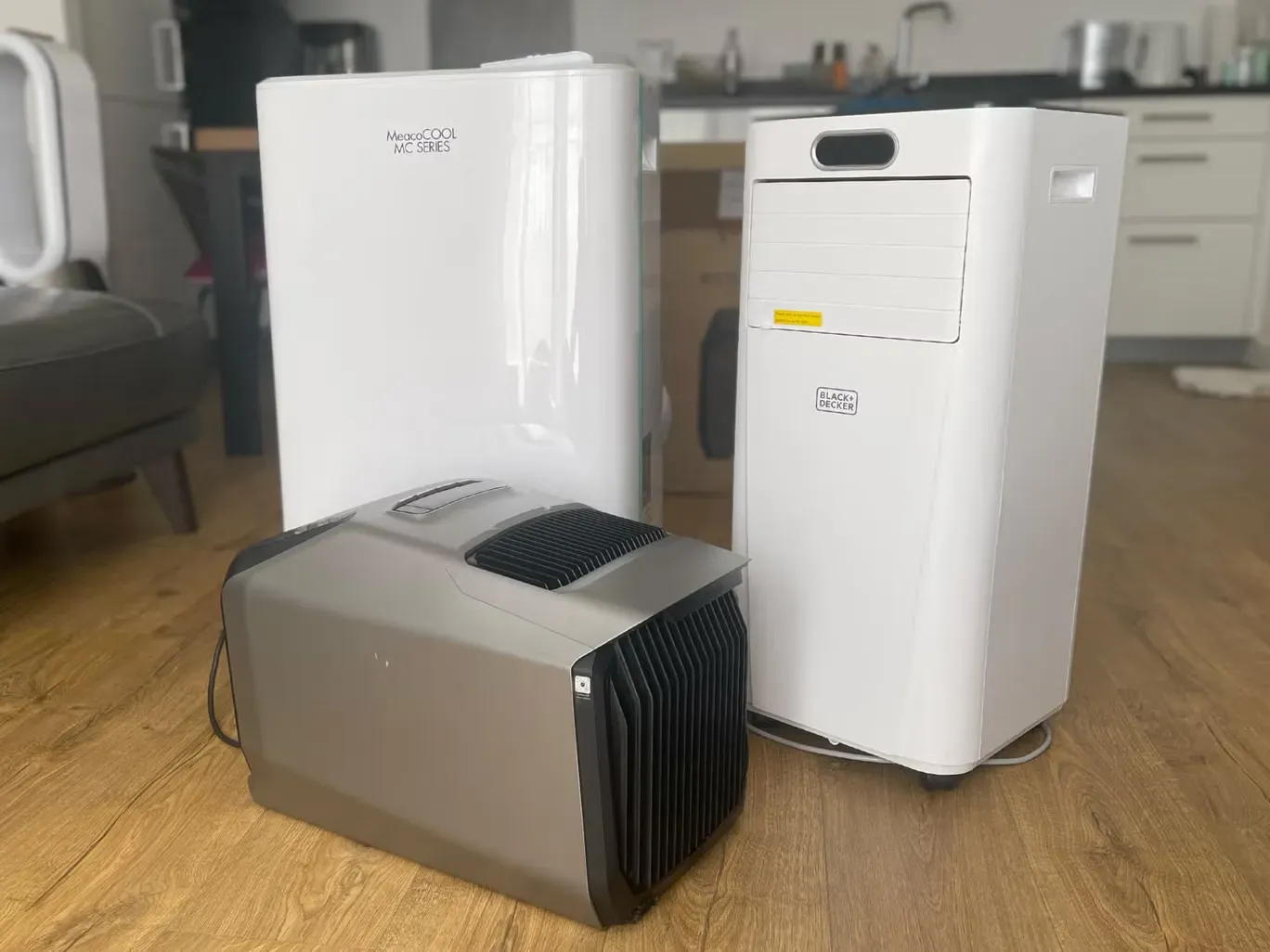 Three air conditioners are sitting on a wooden floor in a living room. Three air conditioners are sitting on a wooden floor in a living room.