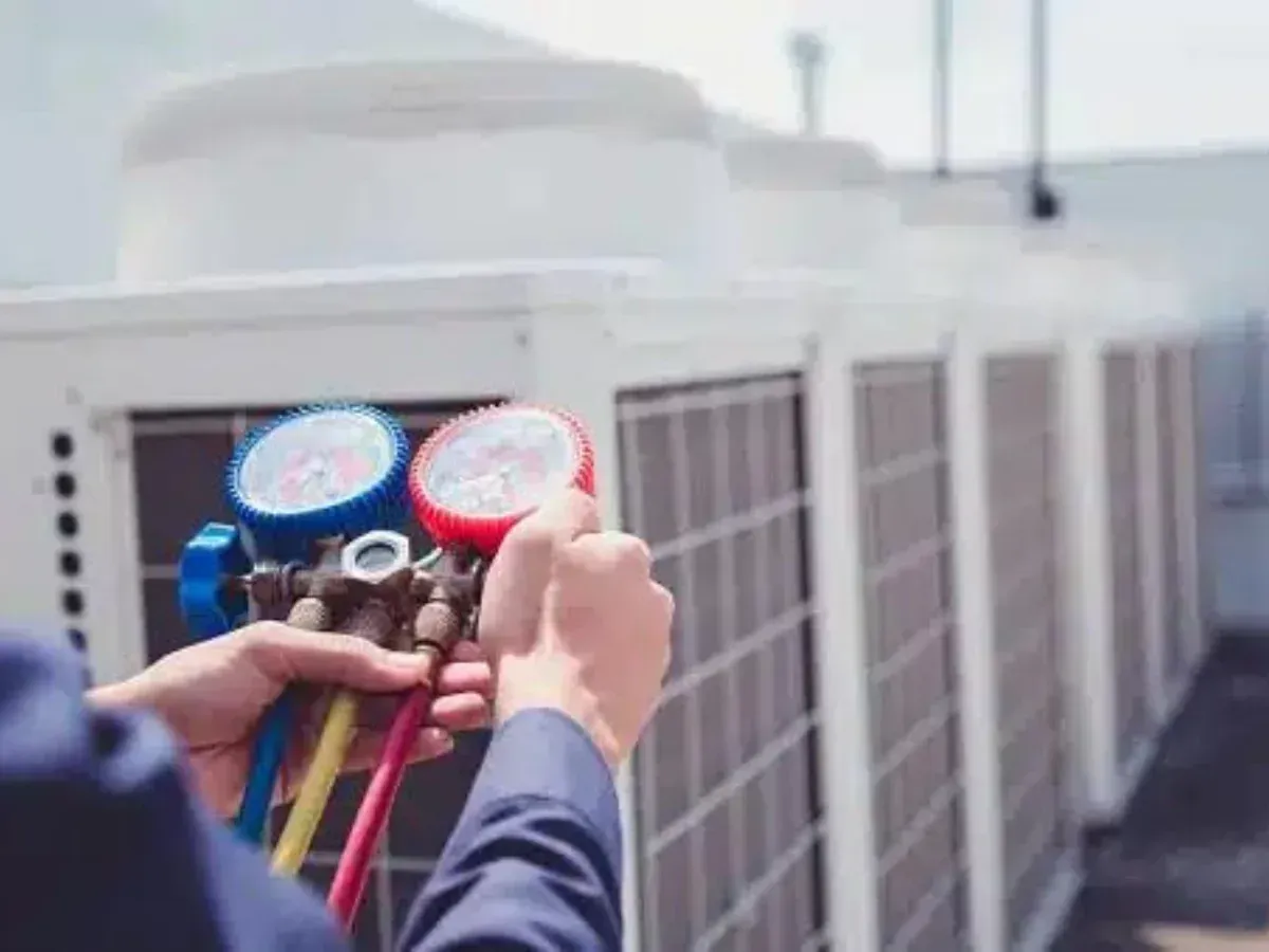 A man is holding a couple of gauges in front of a row of air conditioners.