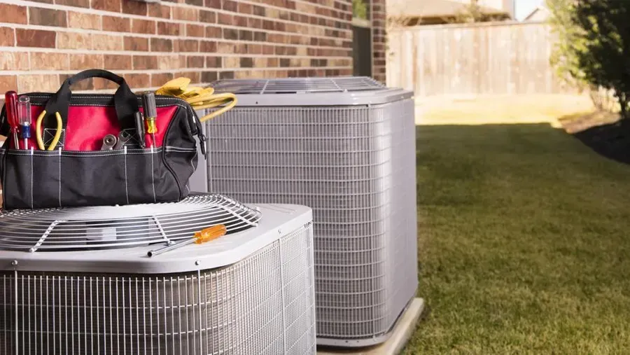 Two air conditioners are sitting next to each other in a backyard. Two air conditioners are sitting next to each other in a backyard.