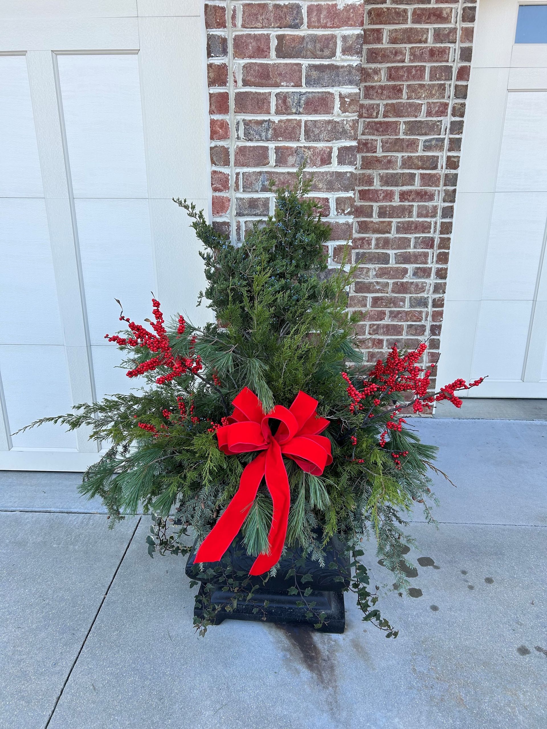 A Christmas Tree in a Planter with a Red Bow in Front of a Brick Building — Jasper, IN — Green Thumb Landscaping and Garden Center 
