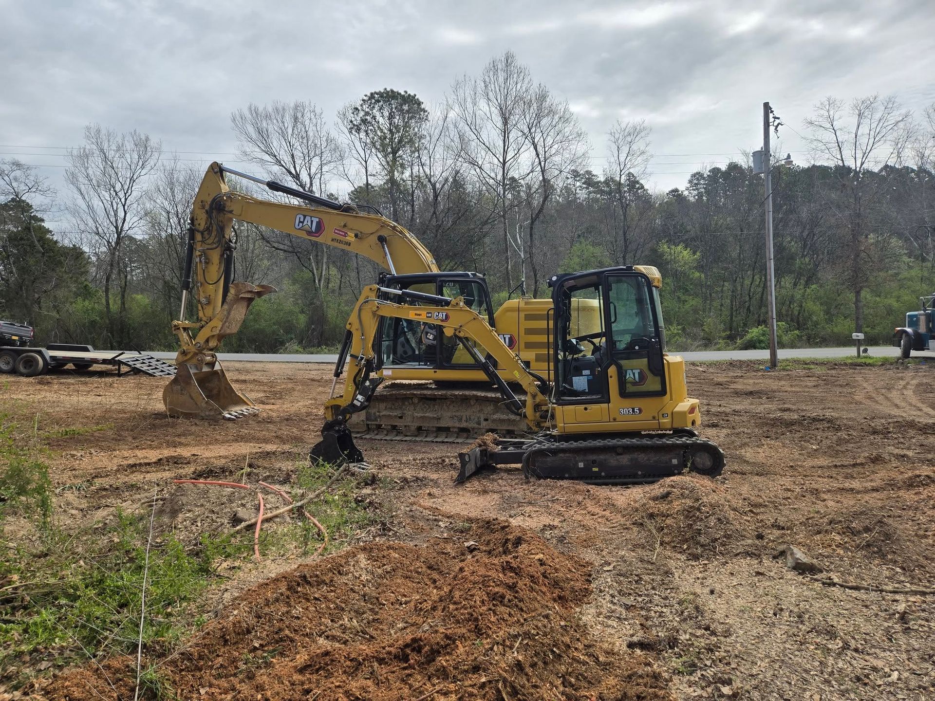 Yellow excavator digging in a muddy construction site with trees in the background