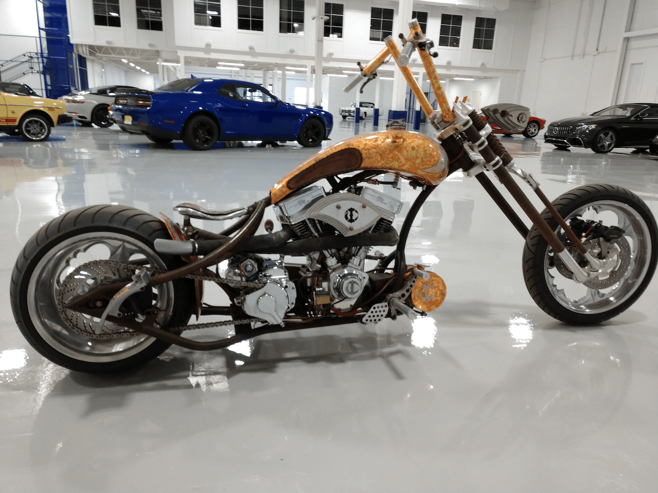 A chopper motorcycle is parked in a garage next to a blue mustang.