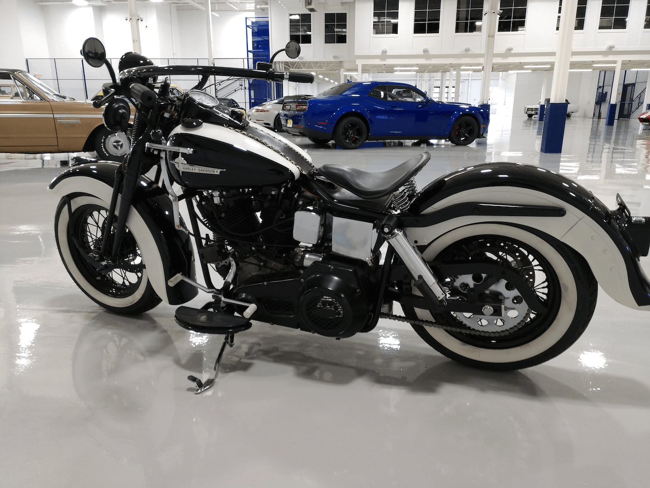 A black and white motorcycle is parked in a garage next to a blue car.