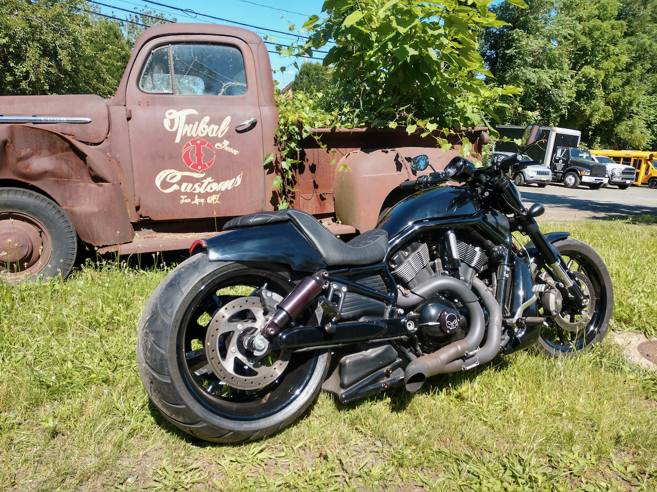 A black motorcycle is parked in front of an old rusty truck.
