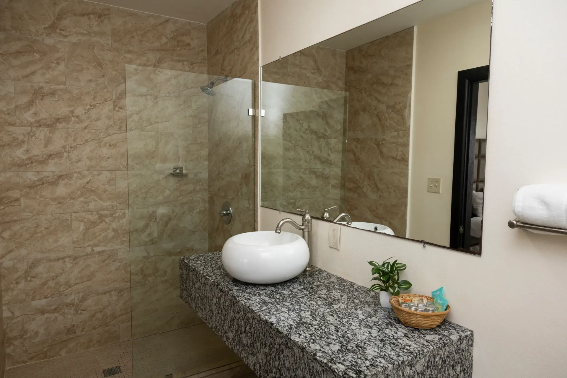 Bathroom with granite countertop, vessel sink, and glass shower enclosure; beige marble walls.