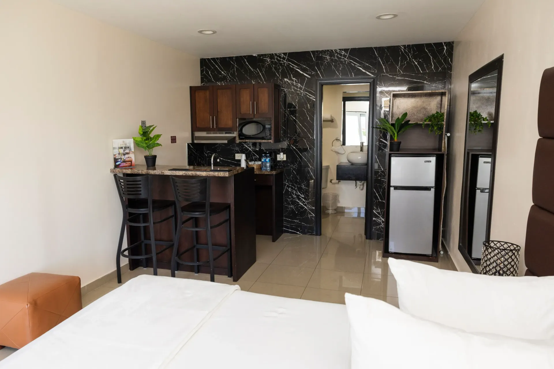Studio apartment with bed, kitchen, bar with stools, and open doorway to the bathroom.