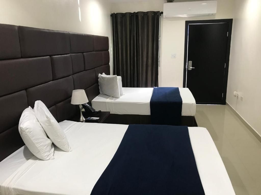 Two beds in a hotel room with white linens, dark blue accents, and a large brown headboard.
