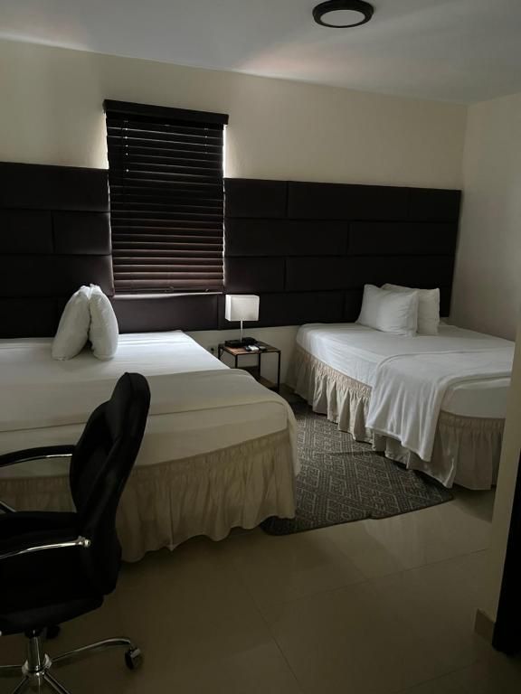 Two twin beds in a hotel room with brown headboards and a window with blinds. A black office chair sits in the foreground.