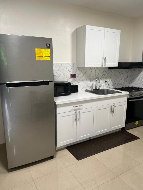 Stainless steel refrigerator, white cabinets, and a sink in a kitchen setting.