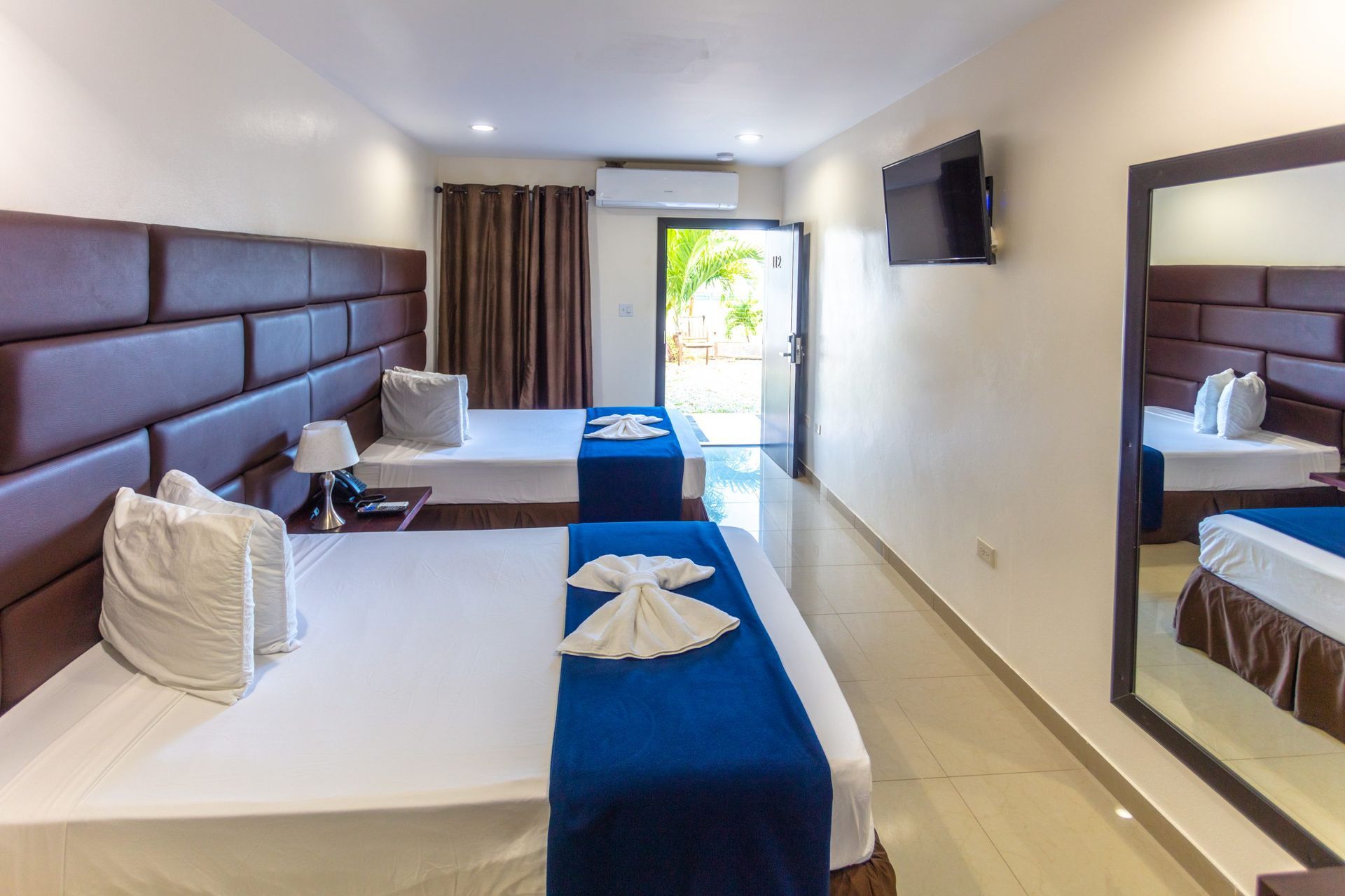 Hotel room with two beds, large mirror, and open door to an outdoor space.