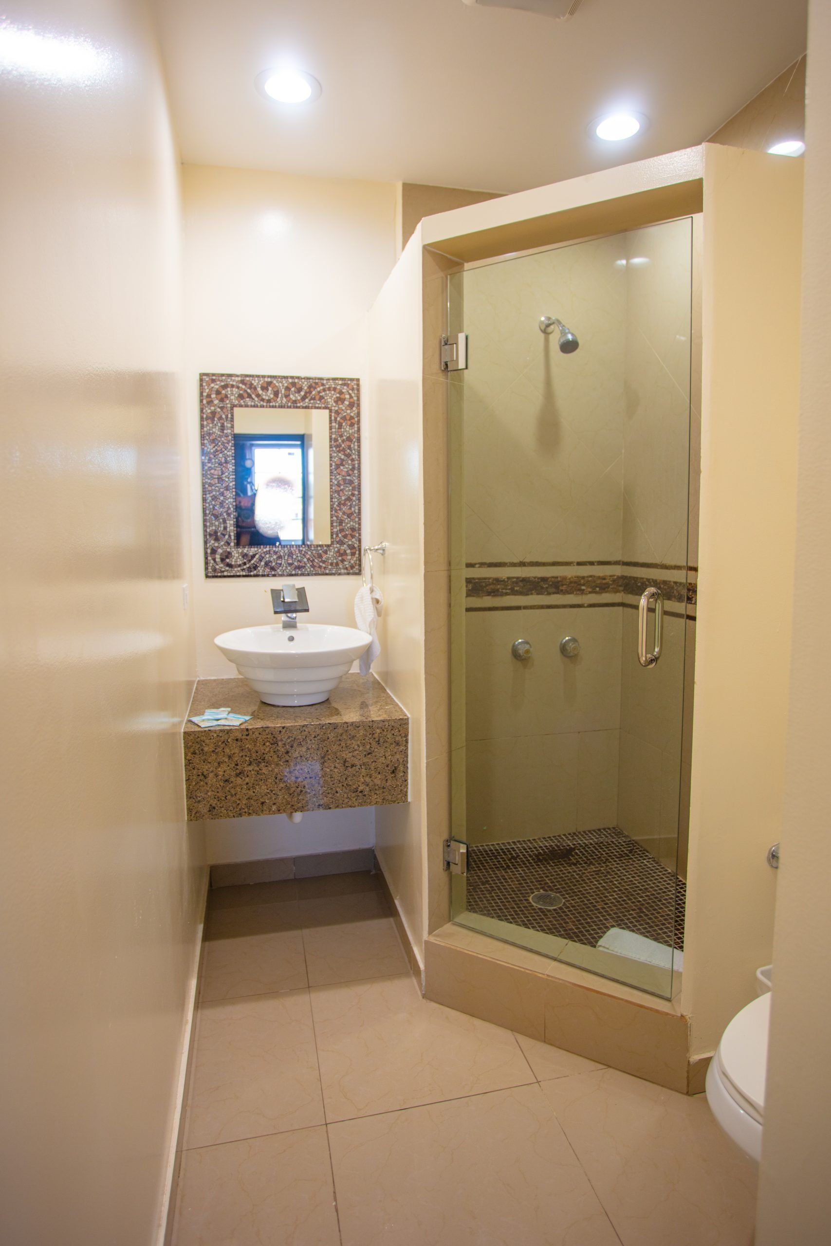 Bathroom with a glass-enclosed shower, vessel sink, and beige walls.