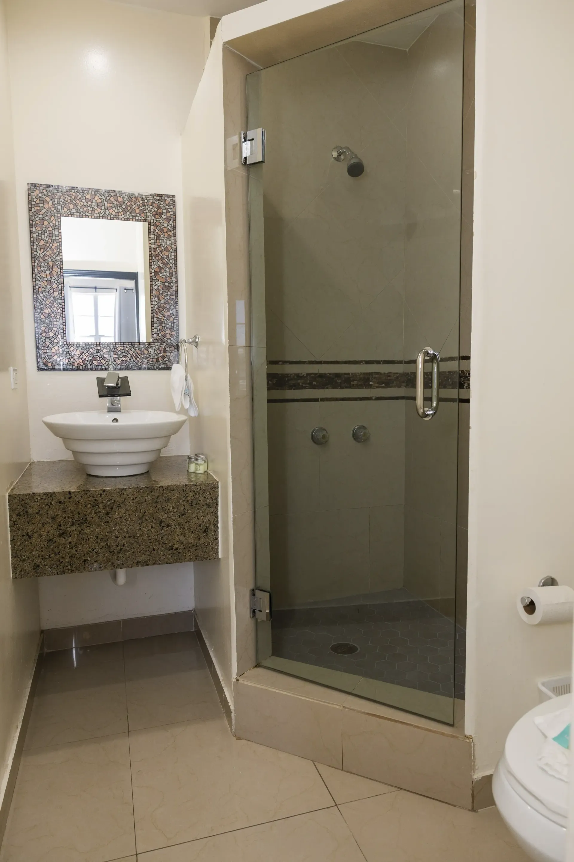 Bathroom with a white sink, mirror, shower, and toilet. Beige tiles and walls.