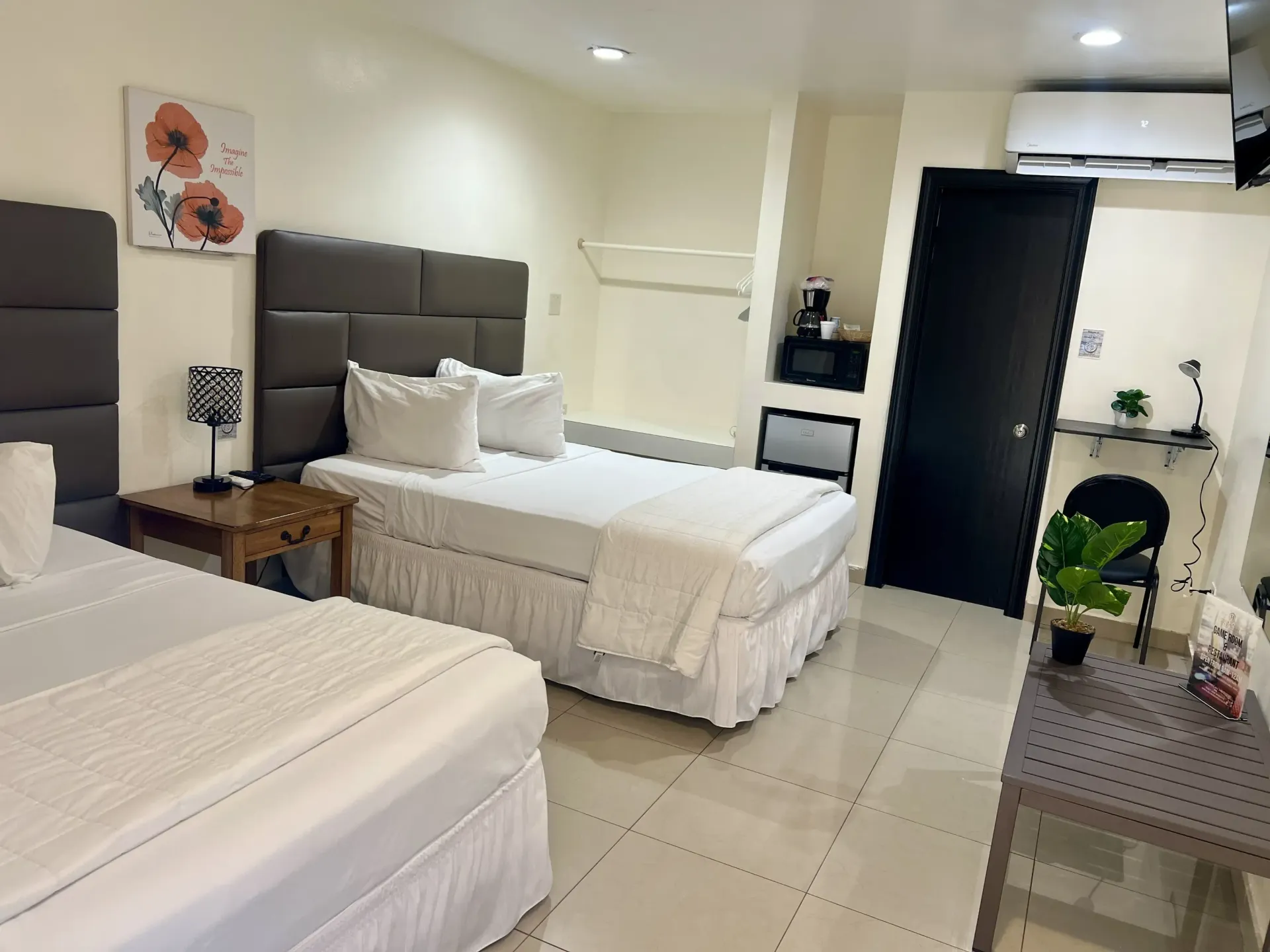 Hotel room with two beds, nightstand, art, television, and table near a door.