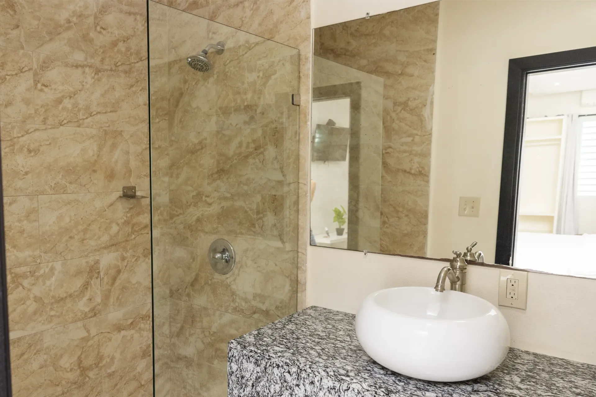 Bathroom with tan marble shower, glass door, white sink on granite counter, large mirror.