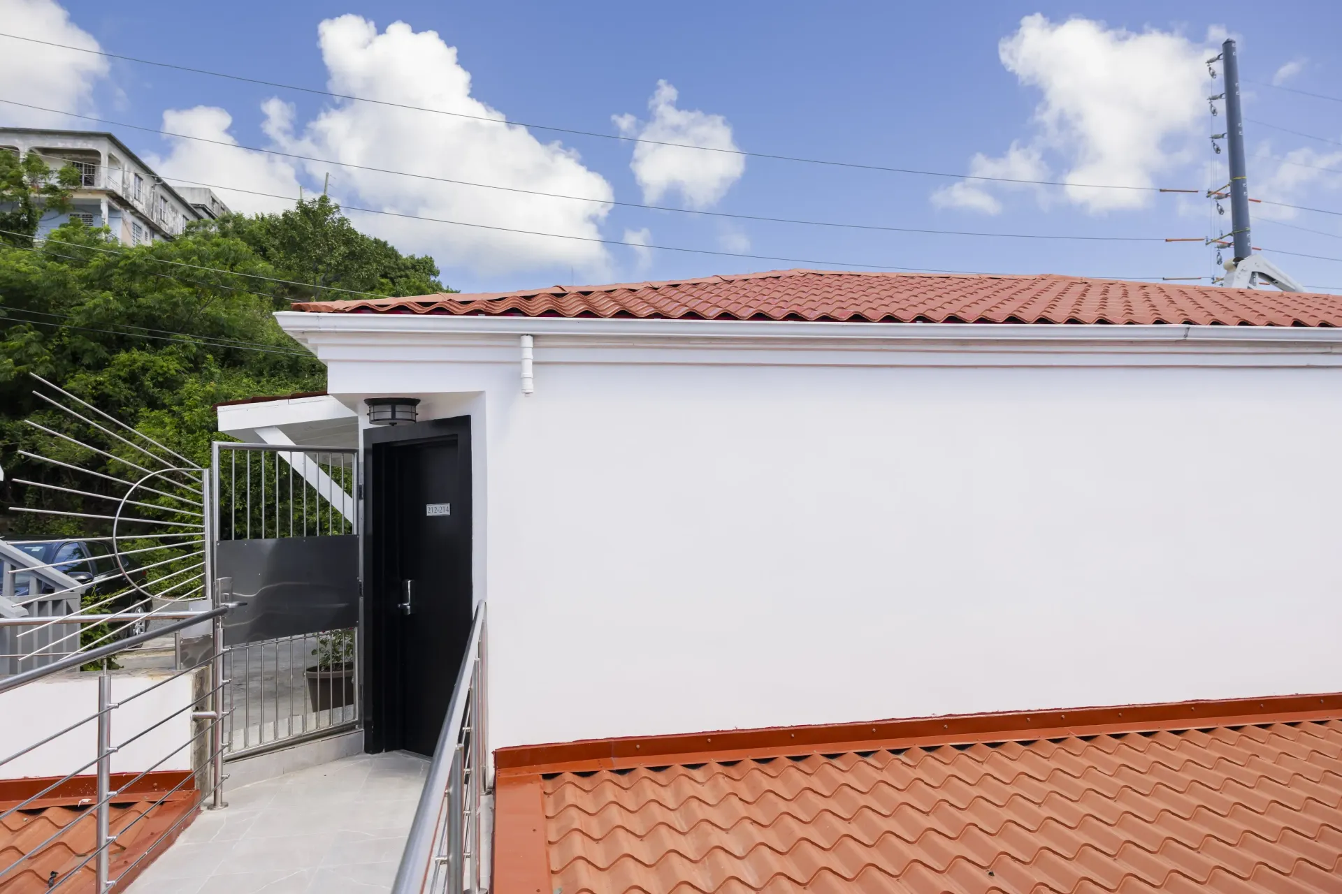 White building with terracotta roof, entrance ramp, blue sky with birds.