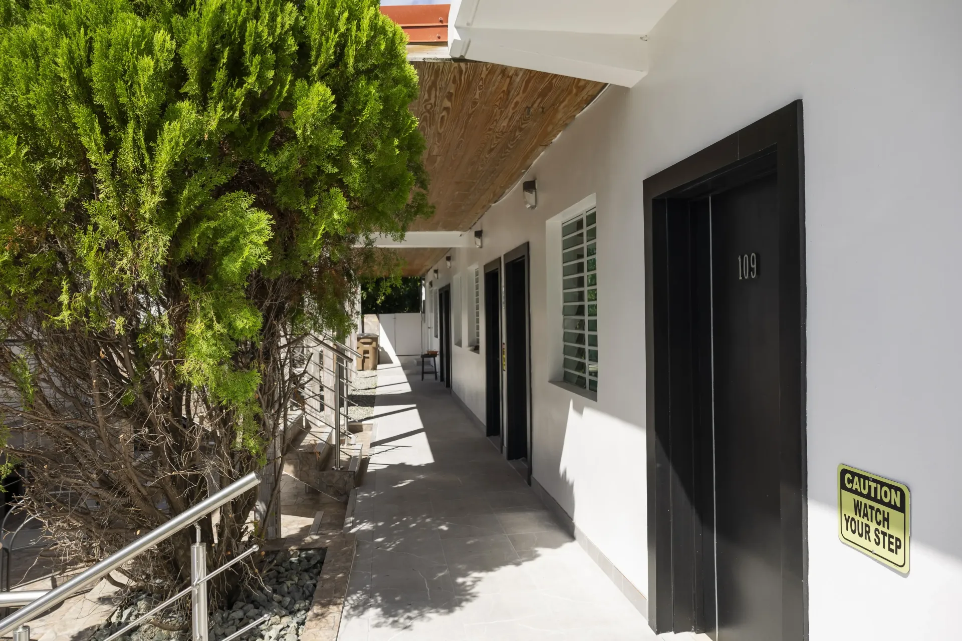 Exterior corridor with black doors and a green shrub.
