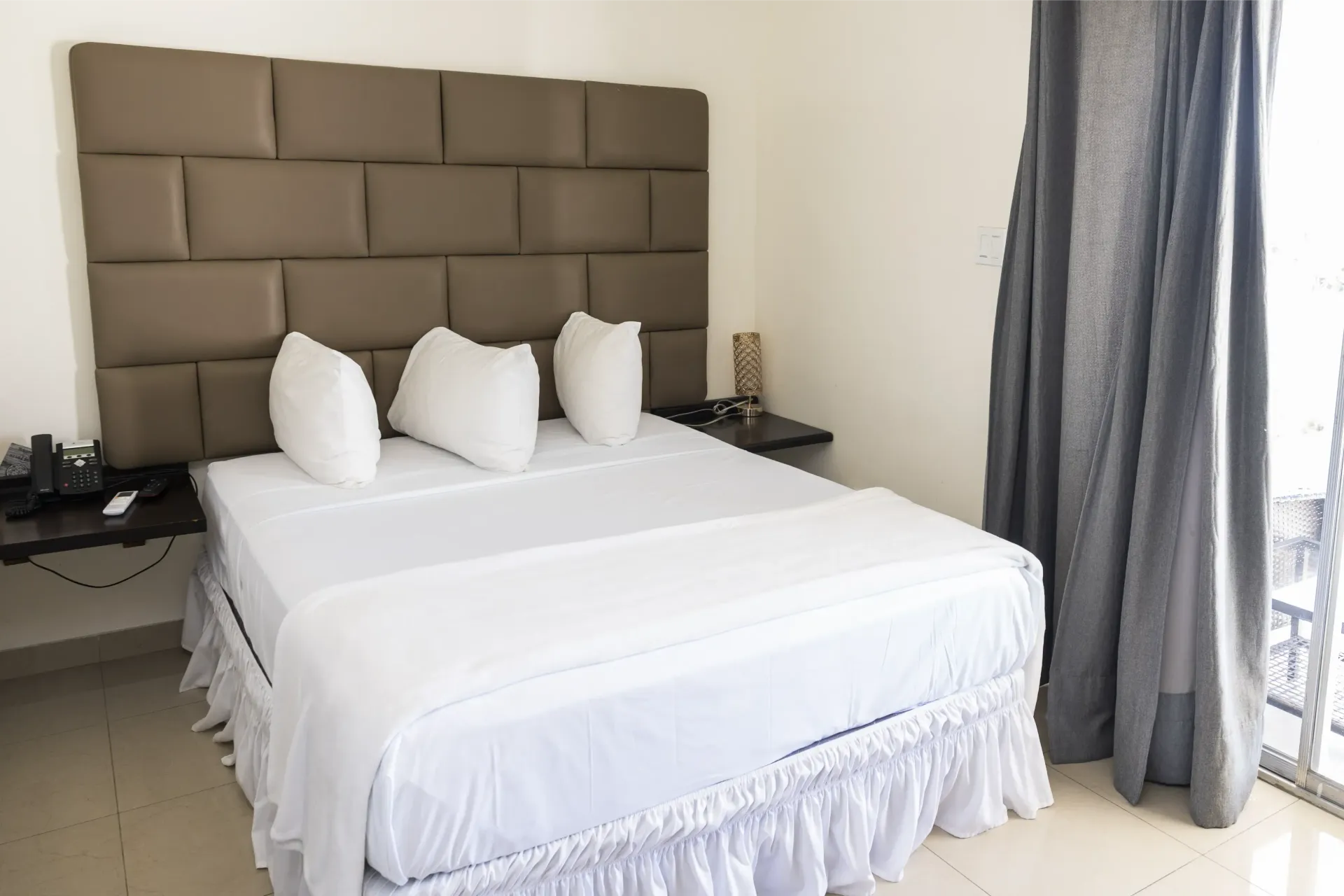 Bedroom with white bedding, brown headboard, and gray curtains.