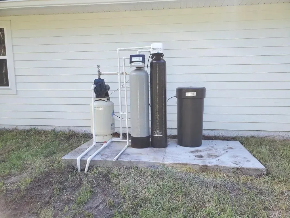 Water softener and filtration tanks on a concrete pad beside a white house exterior