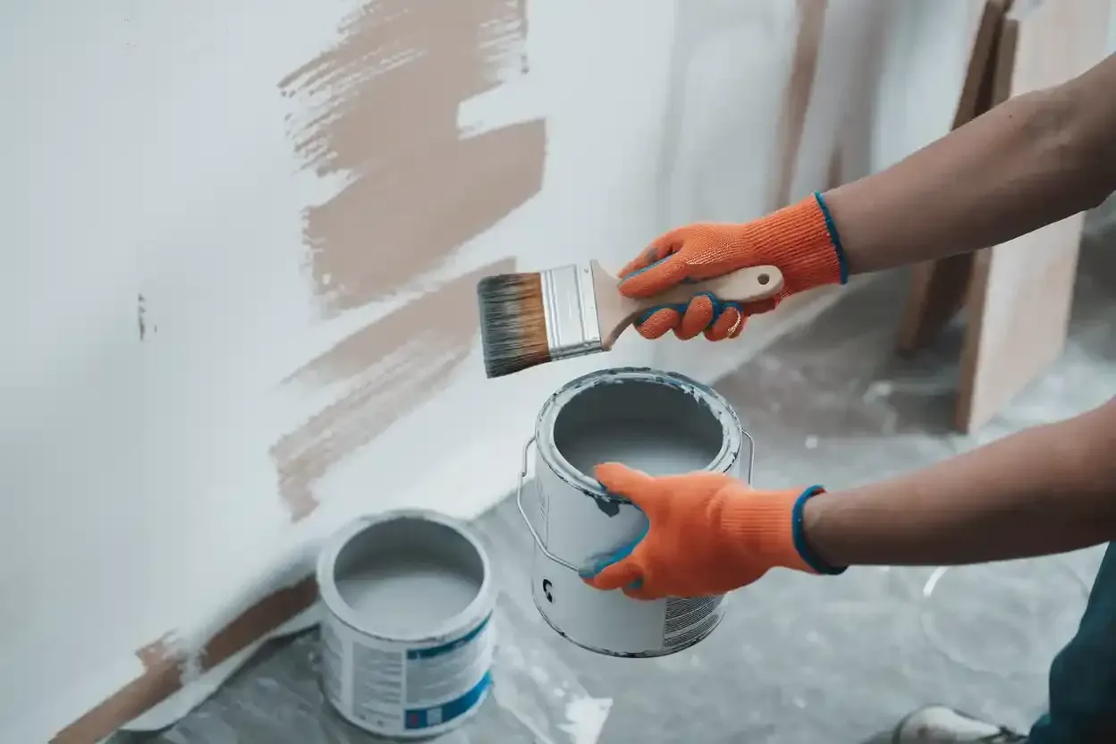 Hands with paintbrush and bucket painting a white wall with beige strokes