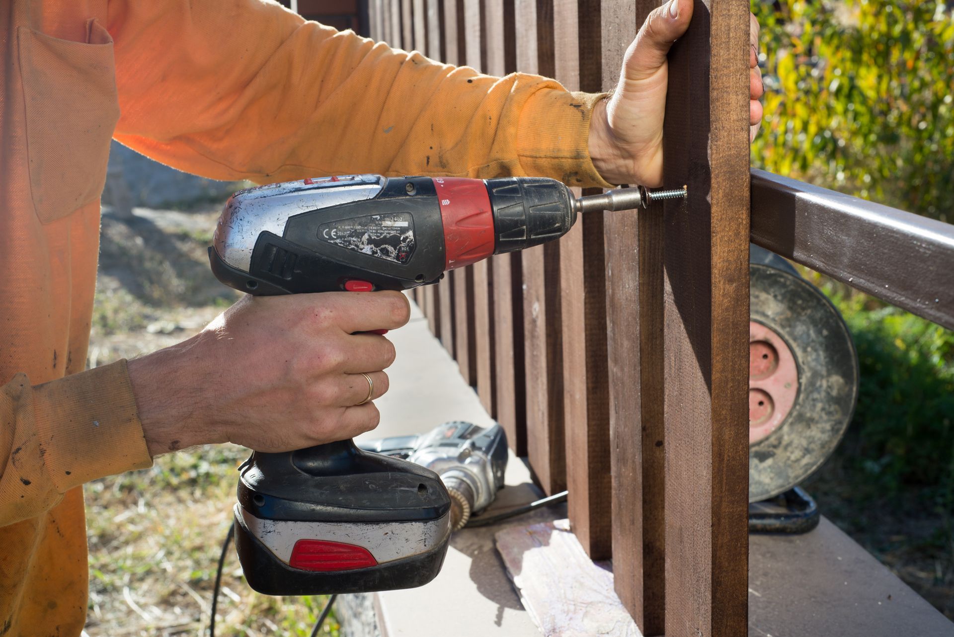 Person drilling a hole in a wooden fence post with a cordless drill outdoors