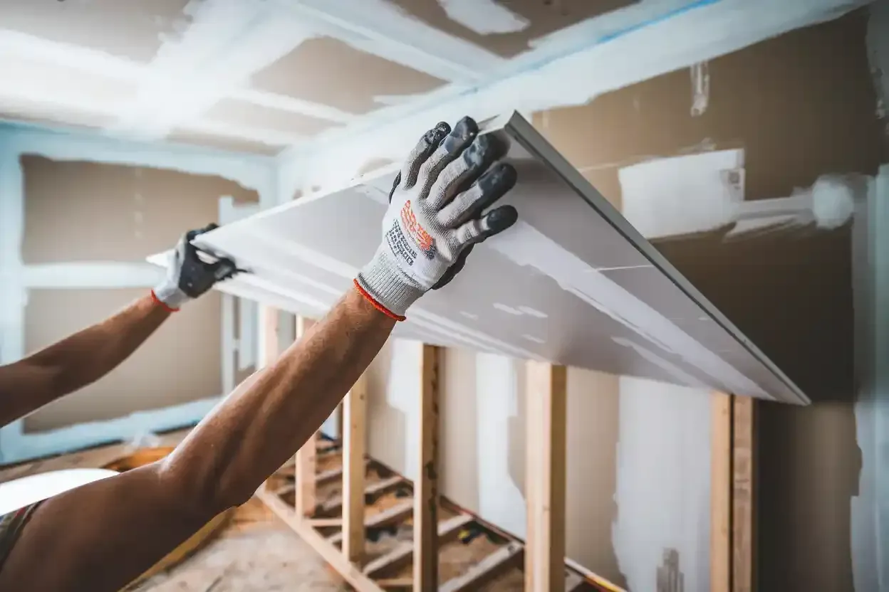 Gloved hands installing drywall on a renovated room ceiling under construction
