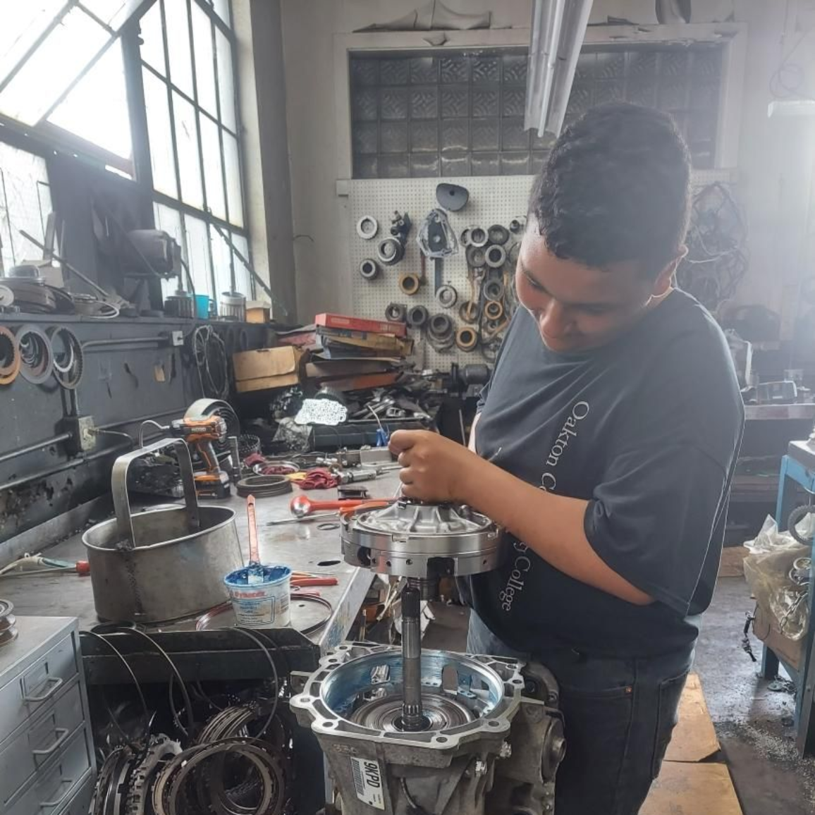 Person assembling engine parts in a workshop, surrounded by tools and metal components.
