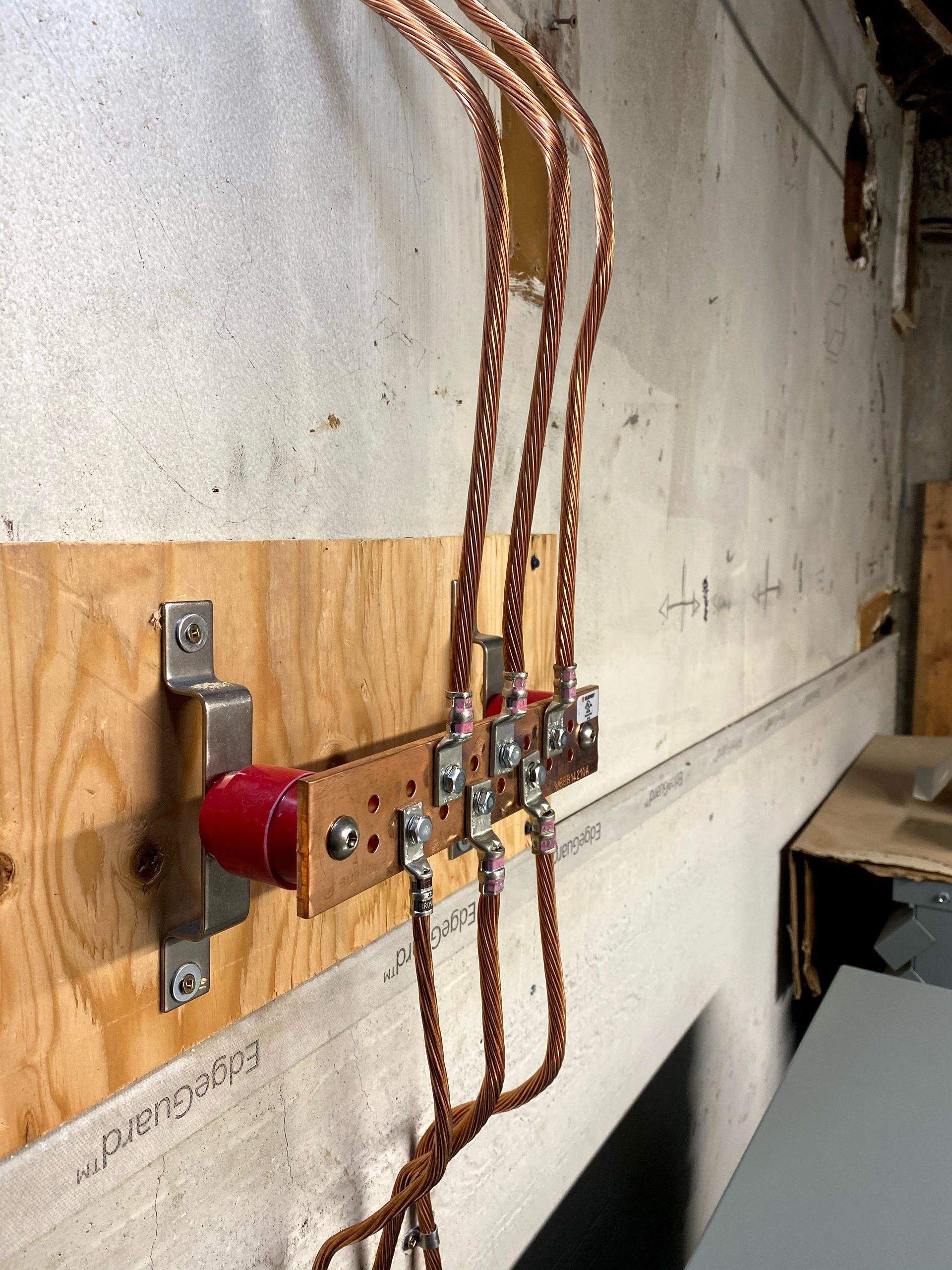 Des câbles électriques en cuivre étaient raccordés à un interrupteur de déconnexion rouge fixé sur du bois, contre un mur en béton.