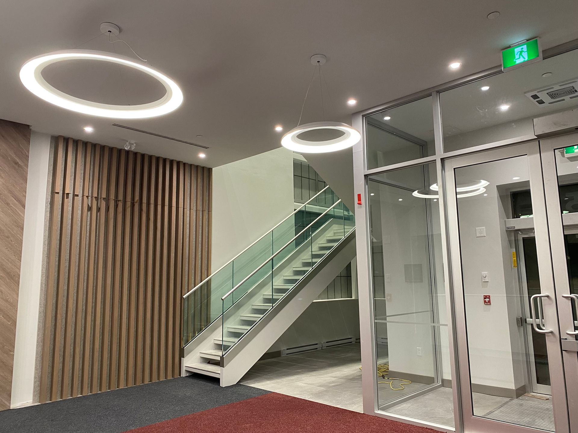 Vue intérieure : hall d’entrée avec escalier, portes vitrées, boiseries et luminaires circulaires.