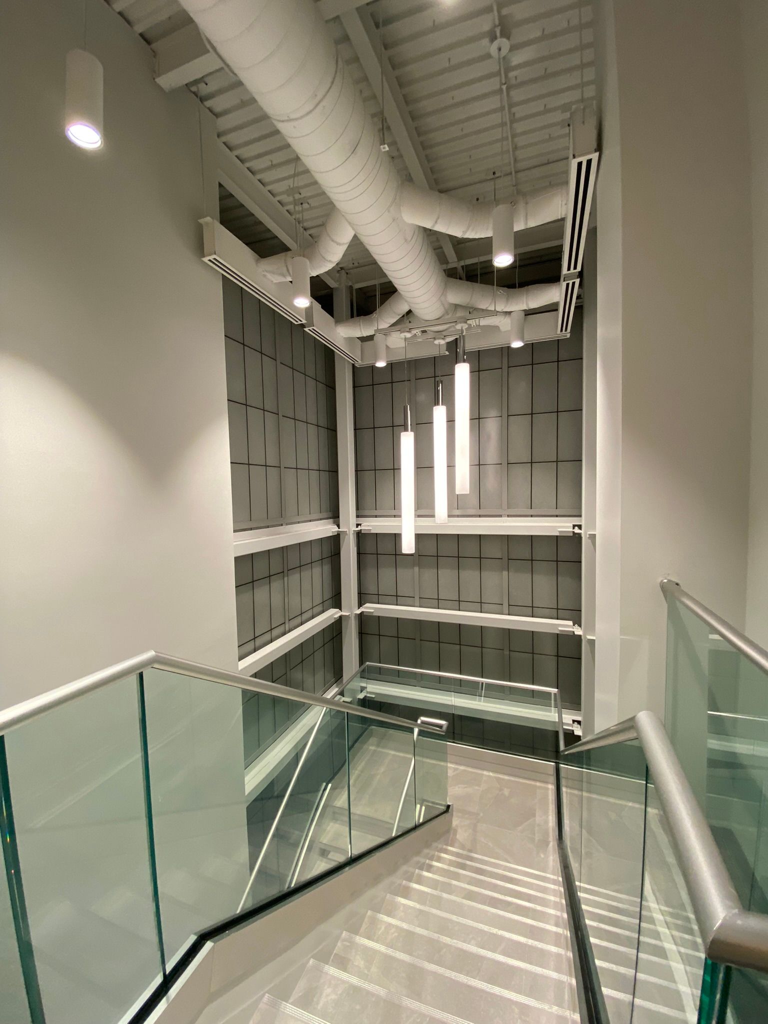 Escalier avec garde-corps en verre et design moderne. Murs et plafond blancs.