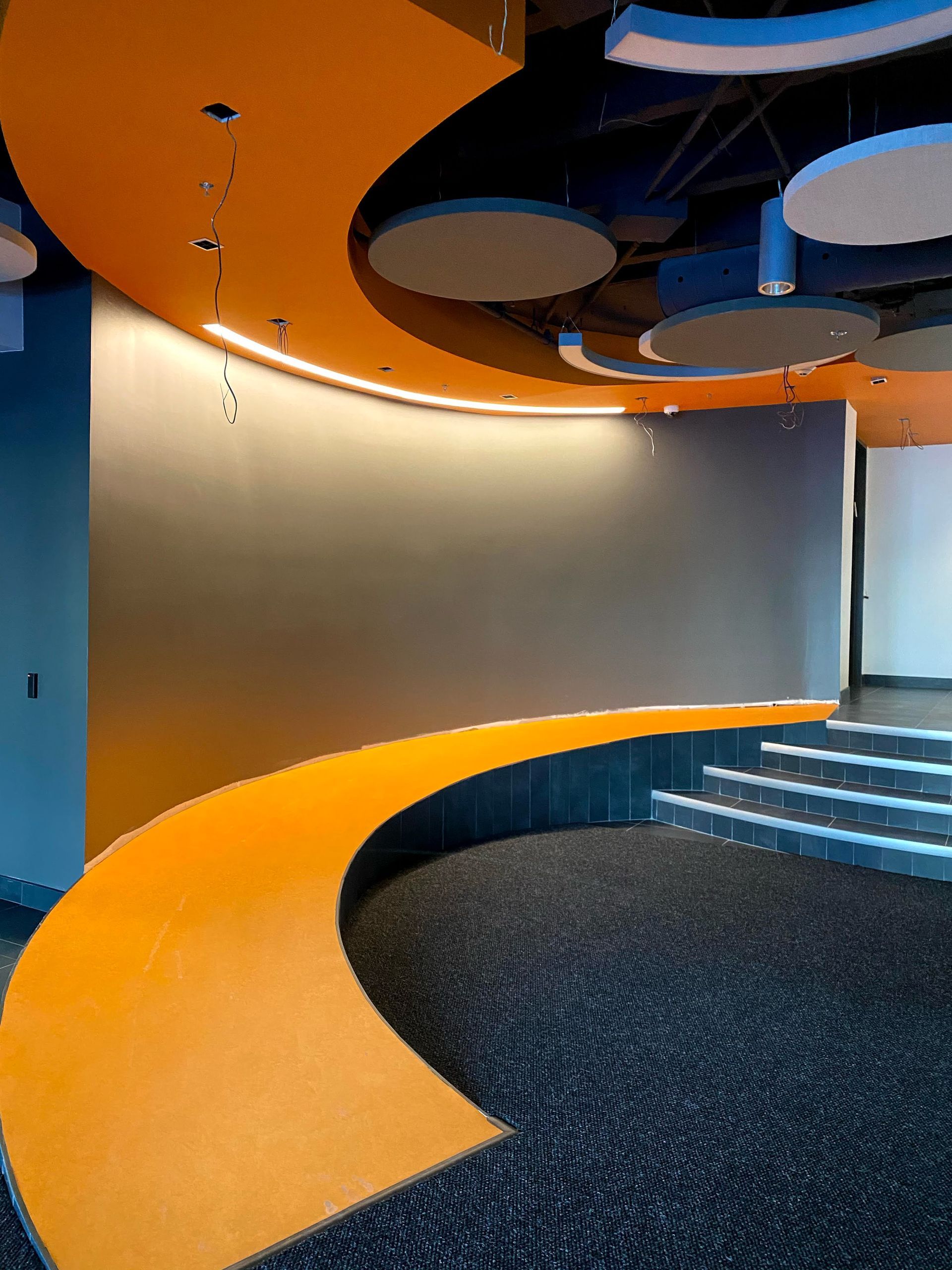 Un chemin incurvé orange dans une pièce aux murs bleus, à la moquette noire et aux plafonniers.