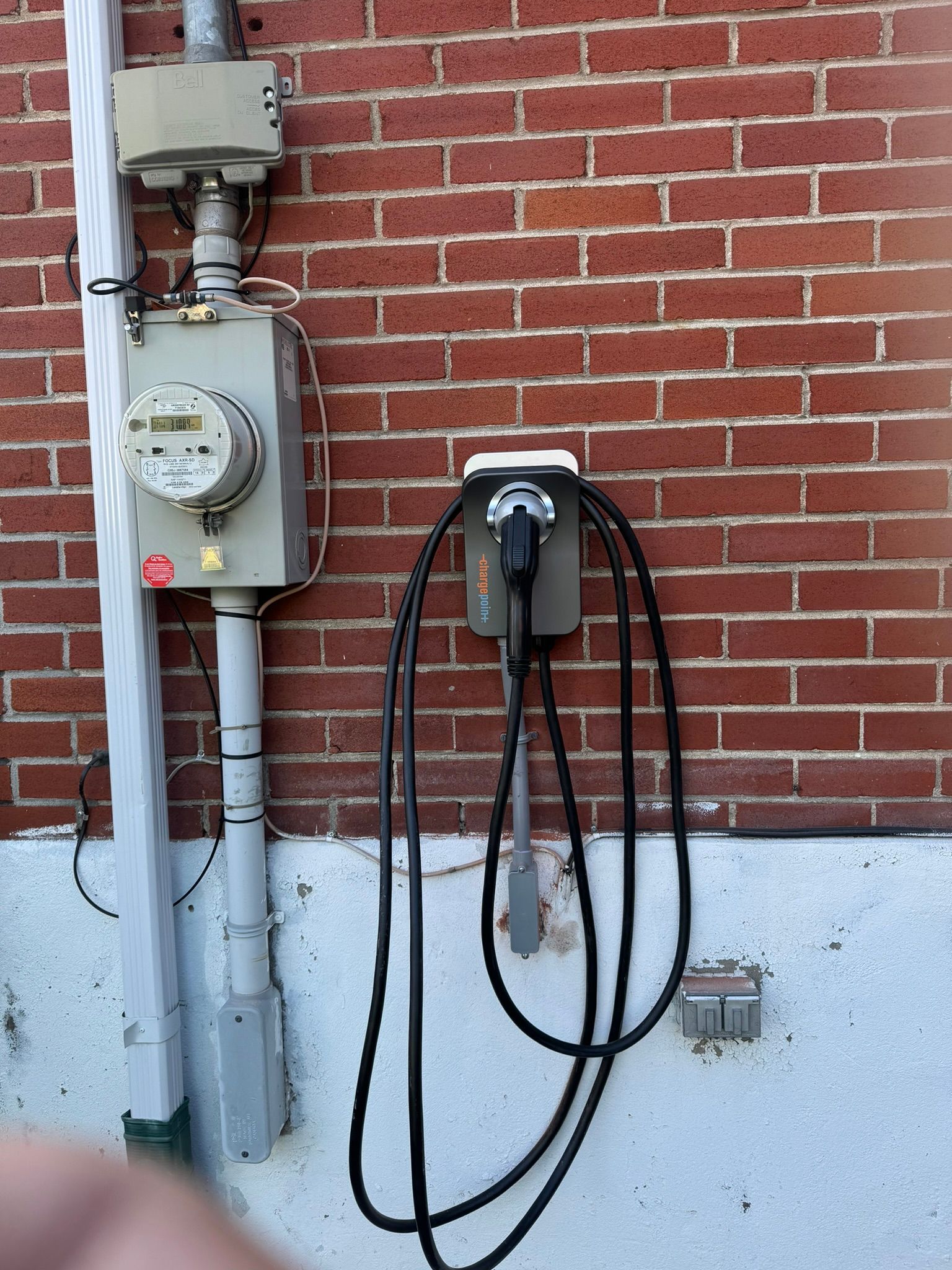 Borne de recharge pour véhicules électriques fixée sur un mur de briques à côté d'un compteur électrique.
