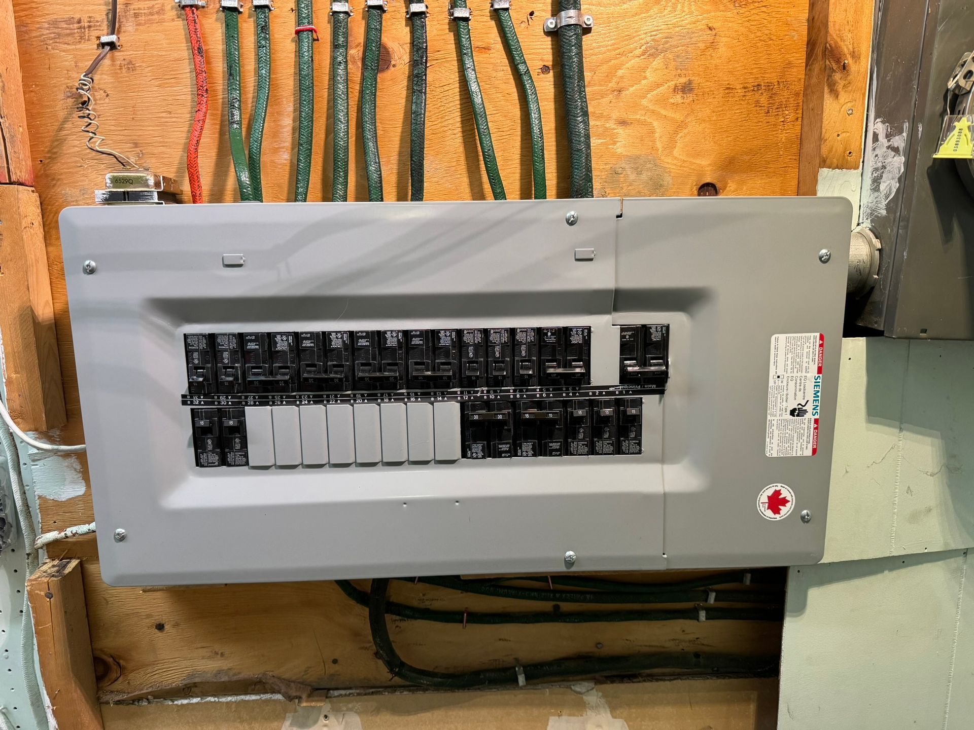 Boîte électrique grise fixée sur un mur en bois, avec plusieurs fils arrivant par le haut.