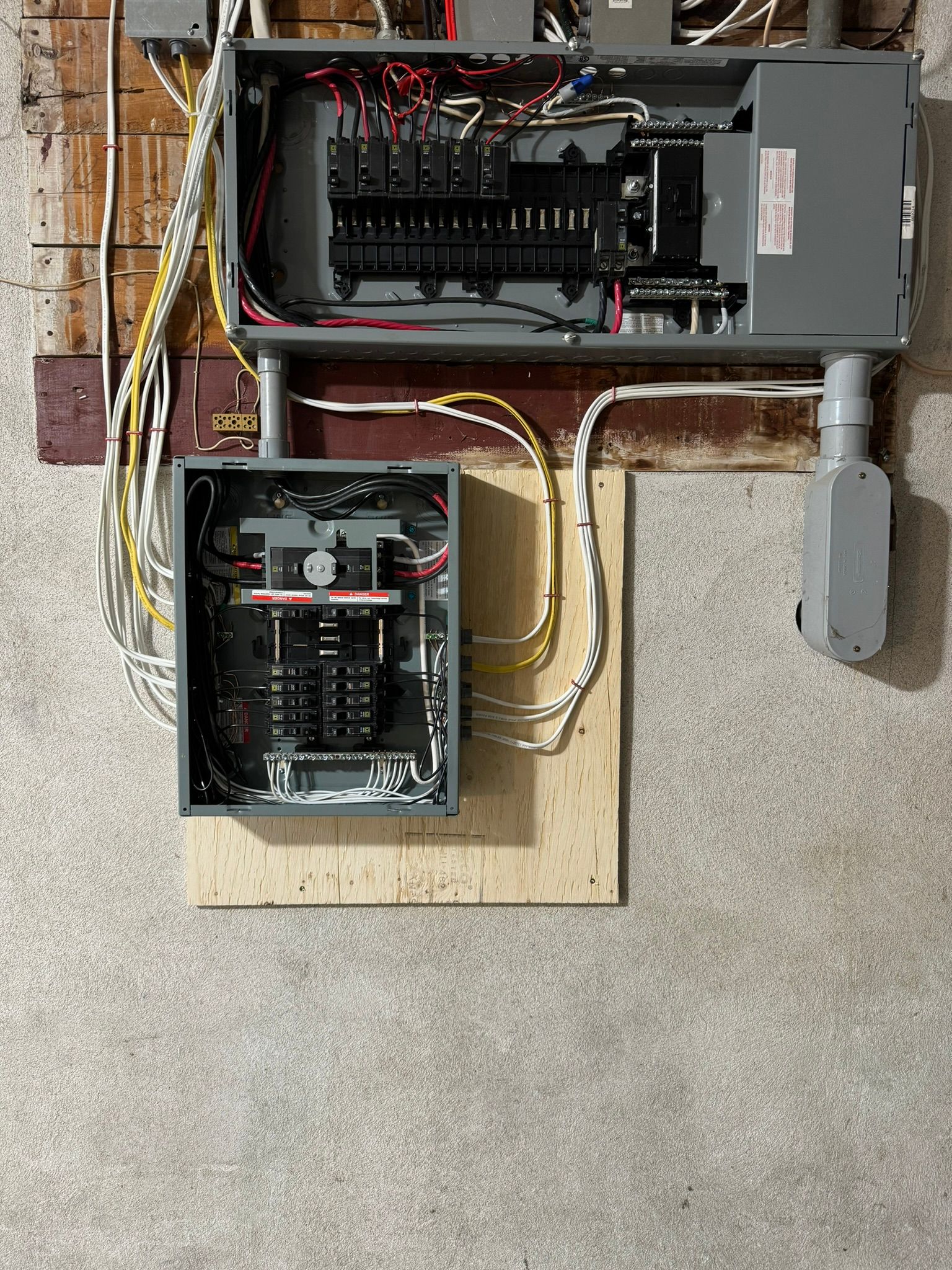 Deux panneaux électriques fixés au mur, avec les conduits et les câbles apparents.