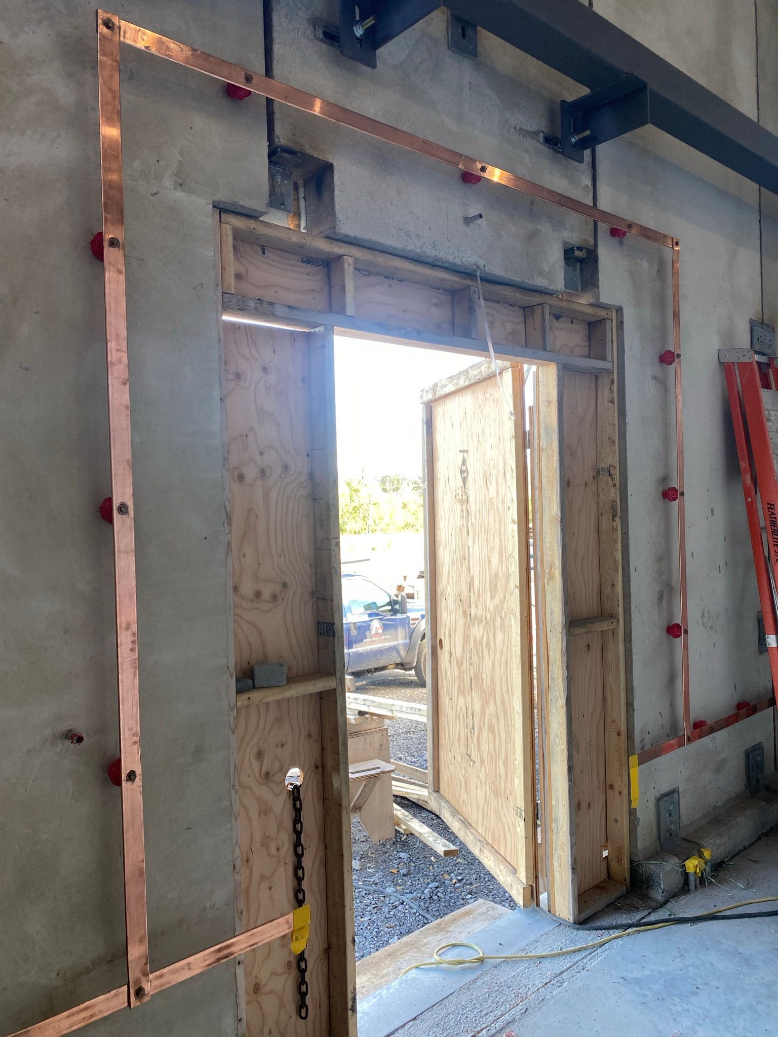 Mise à la terre en cuivre installée autour d'une porte dans un mur en béton.