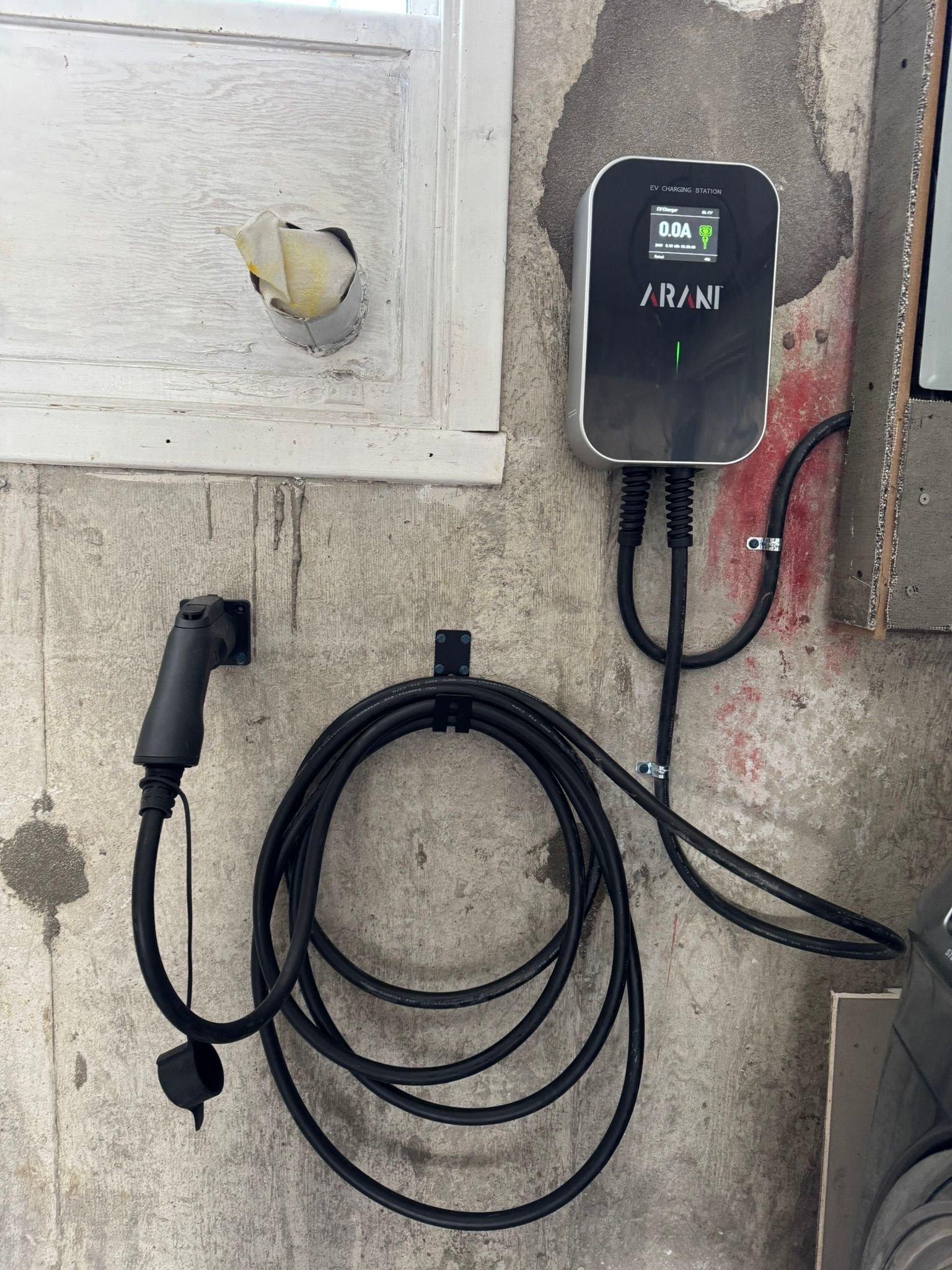 Borne de recharge pour véhicules électriques fixée sur un mur en béton ; câble de recharge enroulé en dessous.