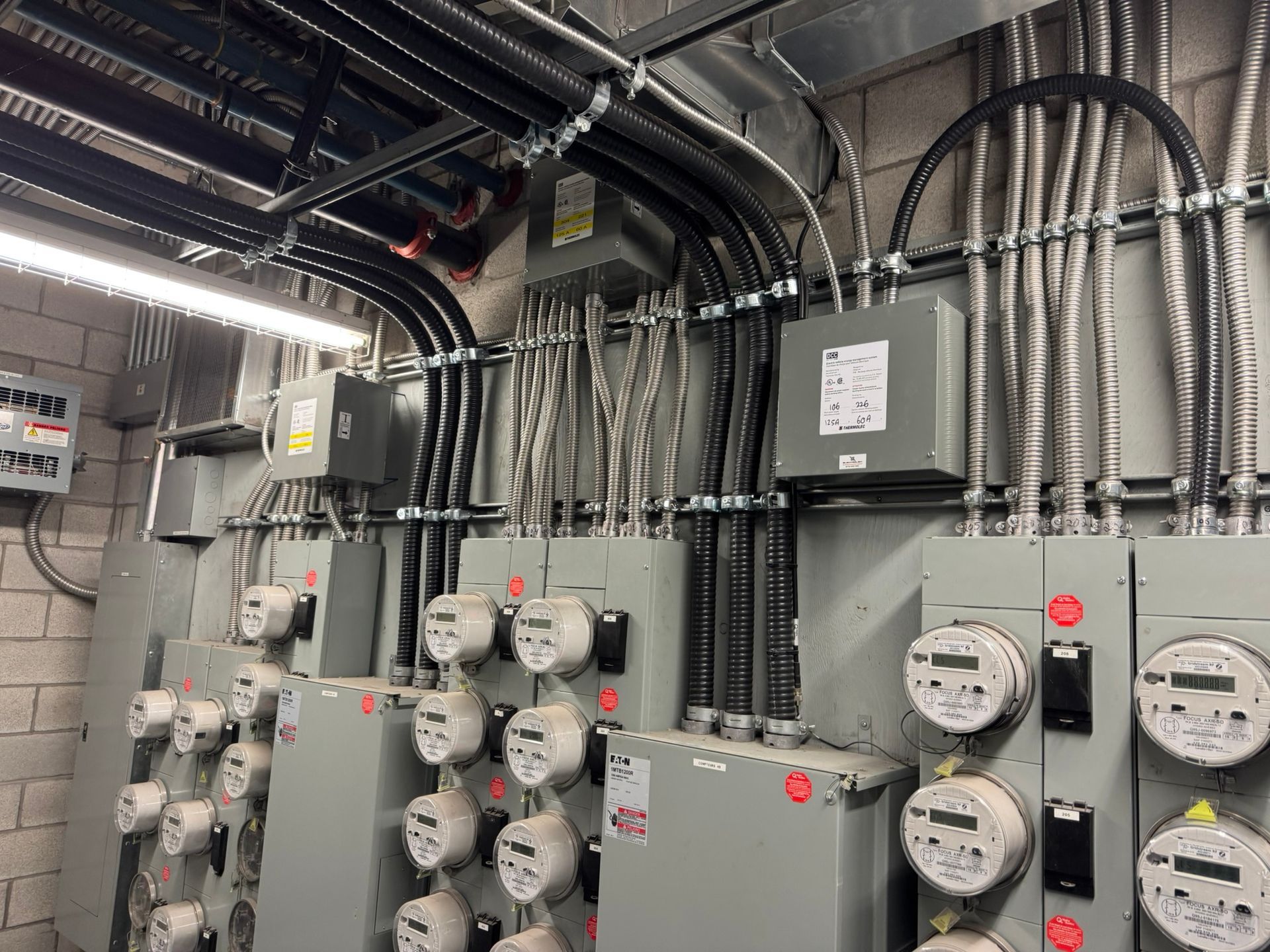 Local technique des compteurs électriques avec plusieurs panneaux gris, compteurs et câblage.