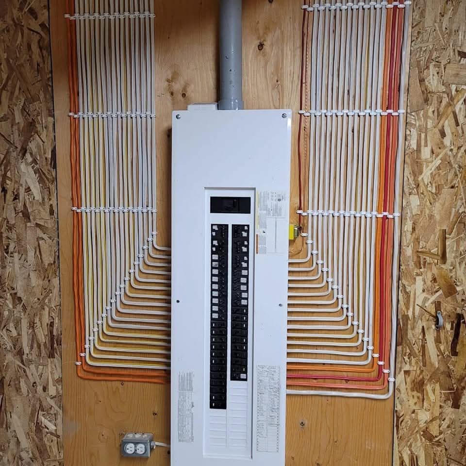 Tableau électrique avec de nombreux fils fixés par des clips blancs sur une surface en bois.