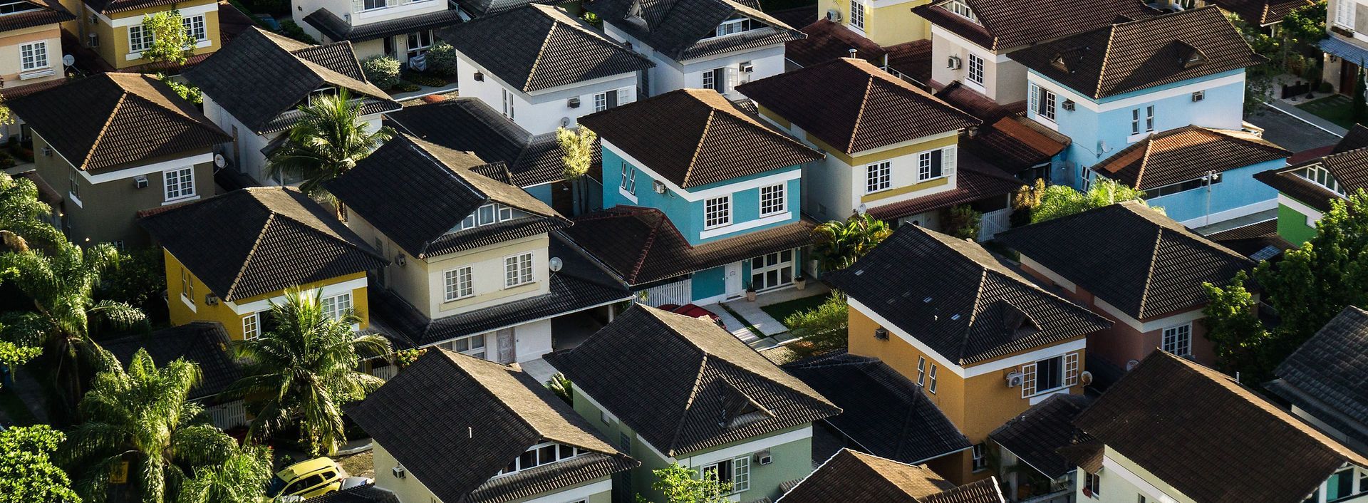 Vue aérienne d'un quartier aux maisons colorées et aux toits sombres, entouré d'arbres.