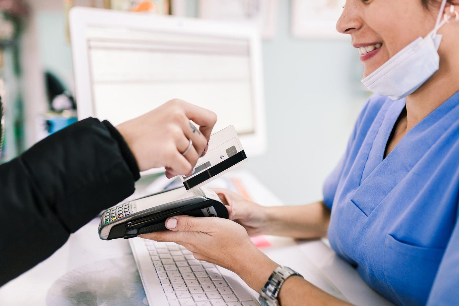 Nurse in blue scrubs accepts a card payment from a customer at a counter