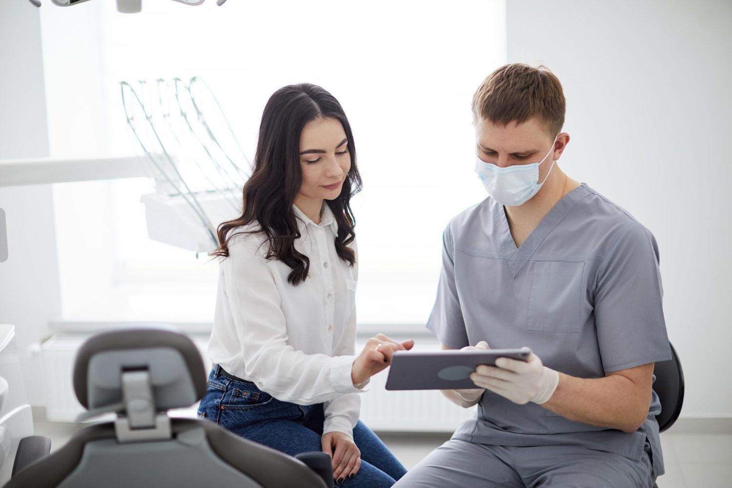 Dentist showing a tablet to a masked patient in a bright clinic office