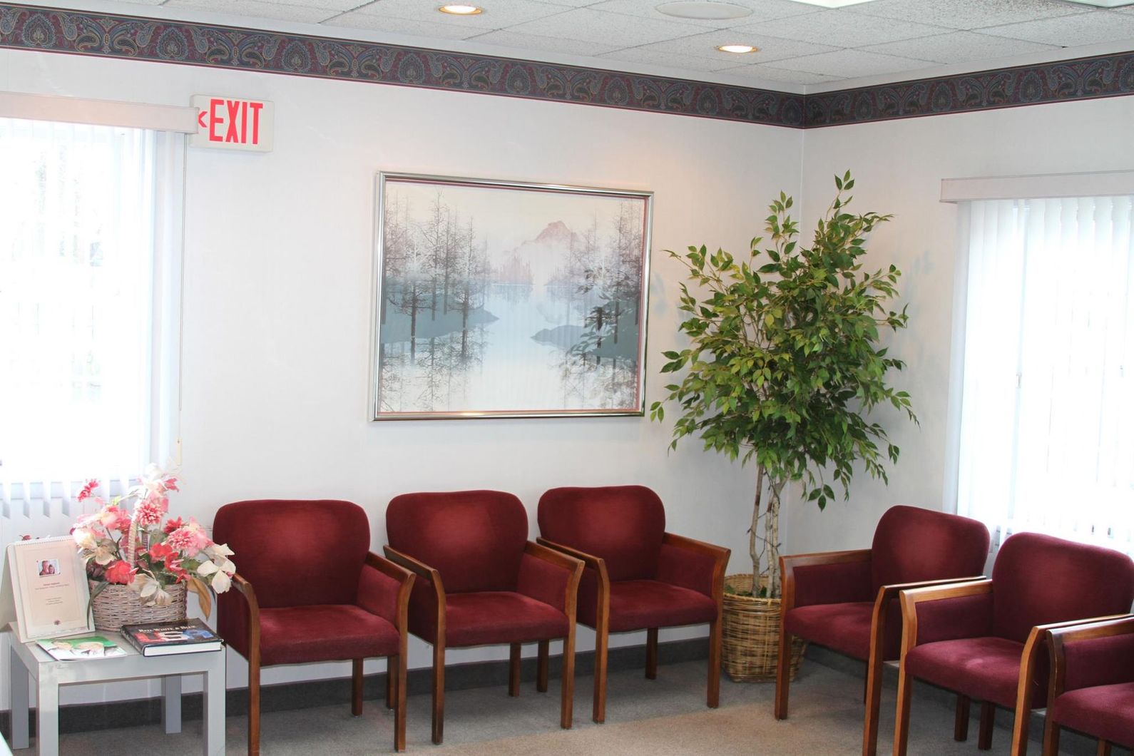 Waiting room with red chairs, floral arrangement, wall art, and a potted tree near bright windows