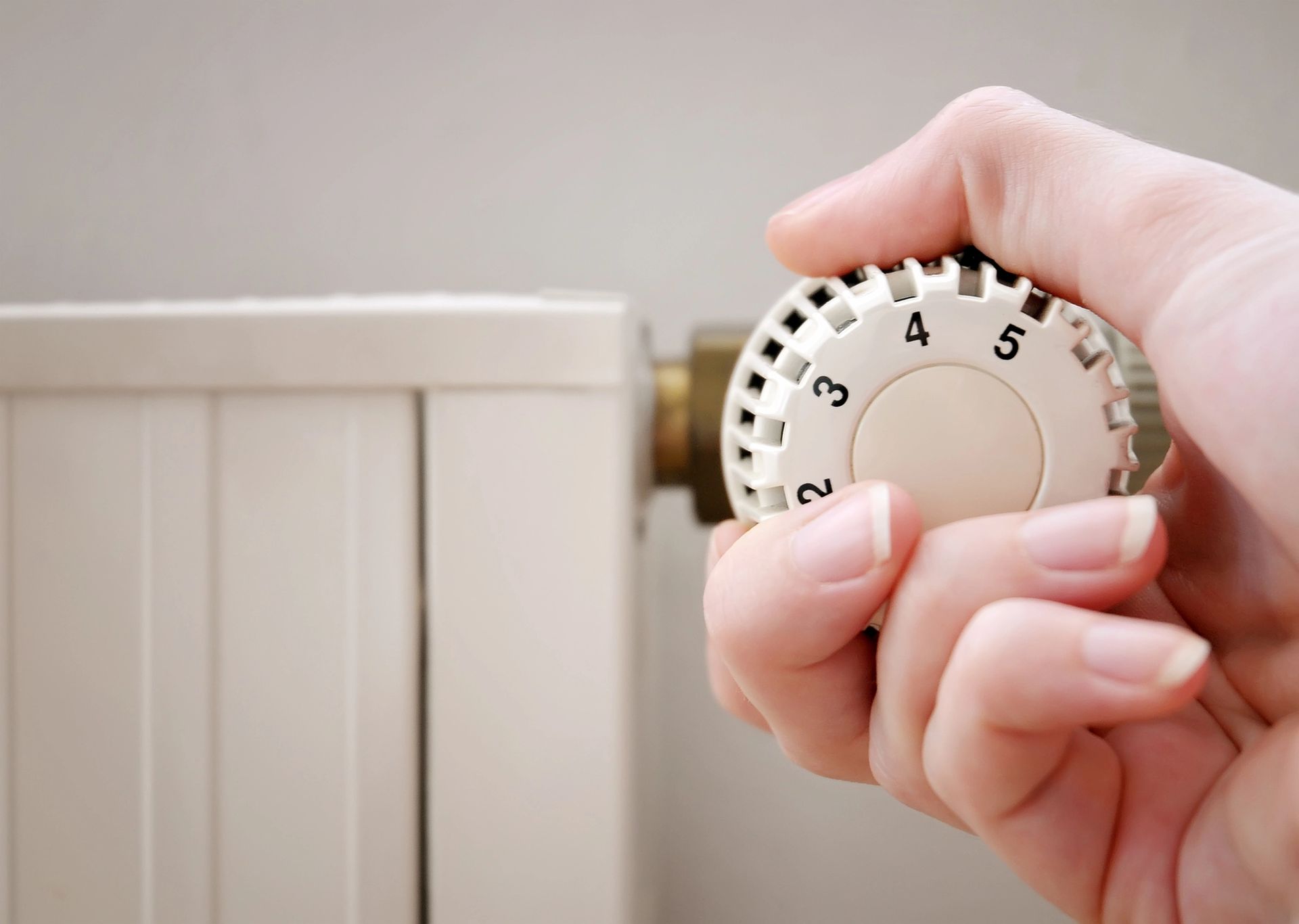 Mano che ruota una manopola bianca del termostato del radiatore per regolare il calore
