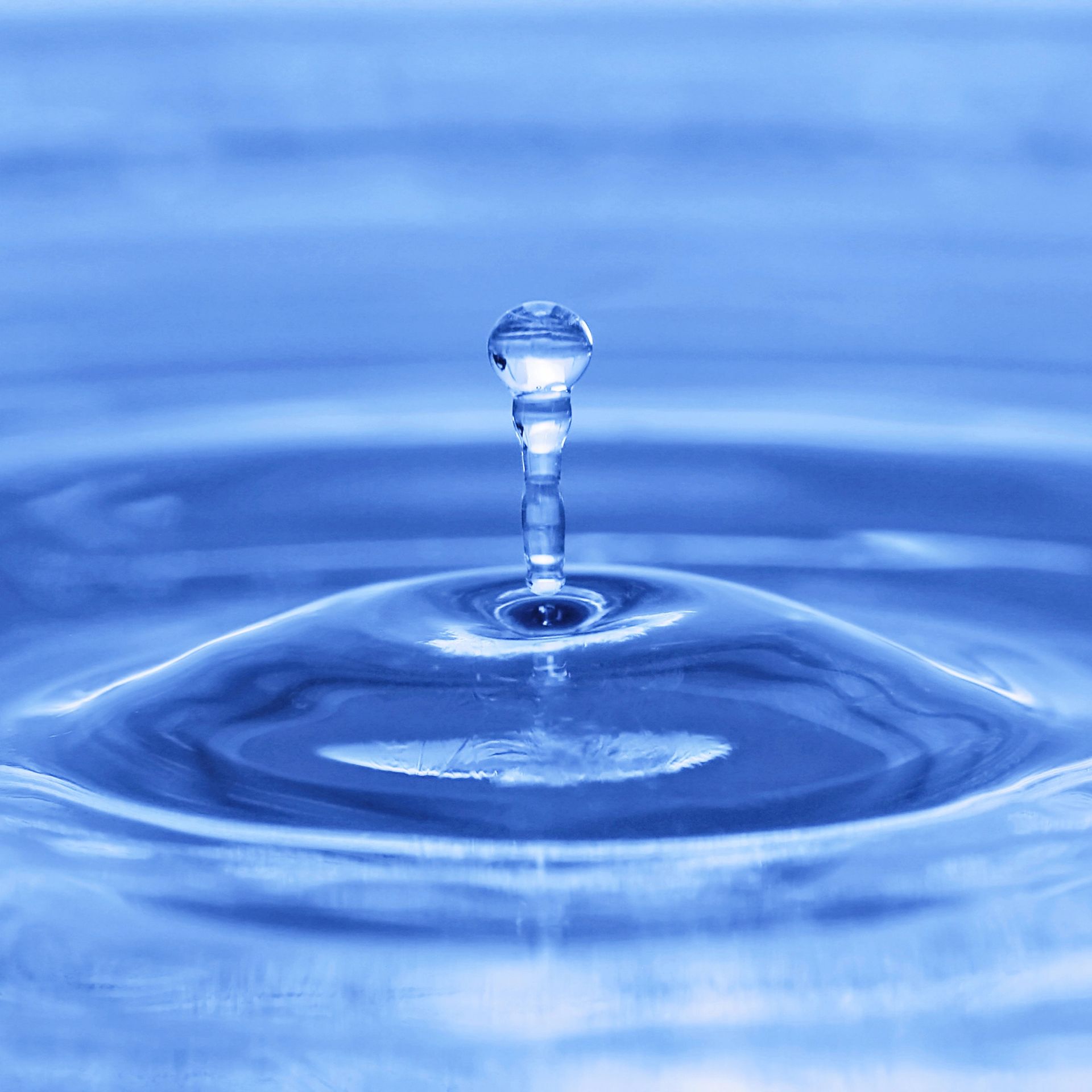 Una goccia d’acqua che schizza su una superficie blu, creando increspature e una colonna centrale