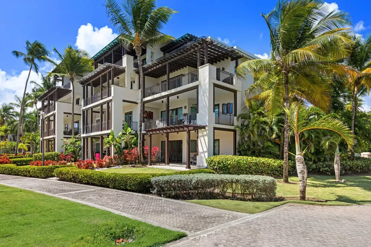 Luxury resort building with balconies, palm trees, and lush tropical landscaping under a bright blue sky
