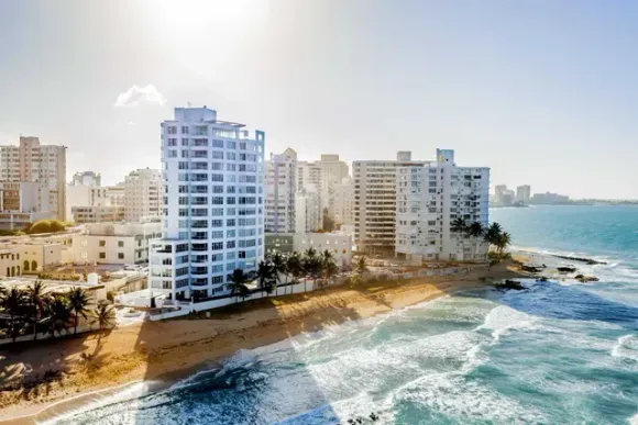 Coastal high-rise apartments beside a sandy beach and turquoise ocean under bright daylight