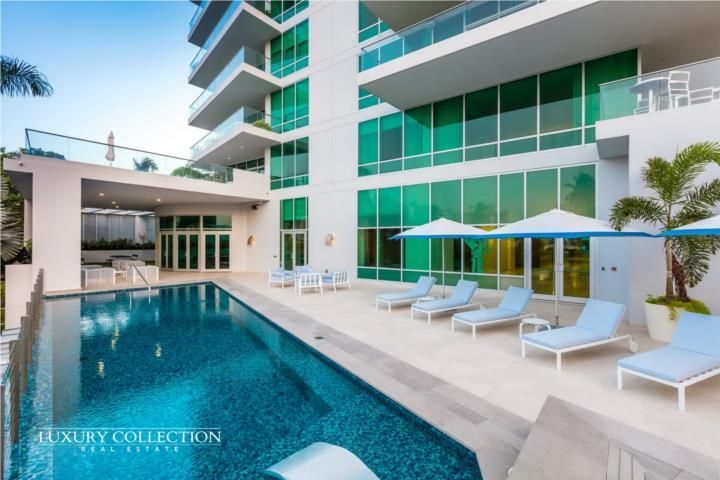 Modern hotel pool with lounge chairs and umbrellas beside a turquoise high-rise building